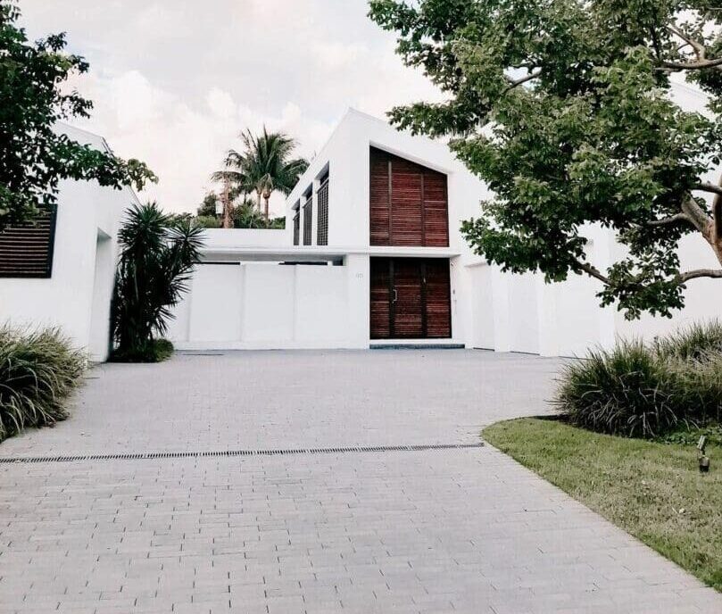 A driveway with a large white house and trees.